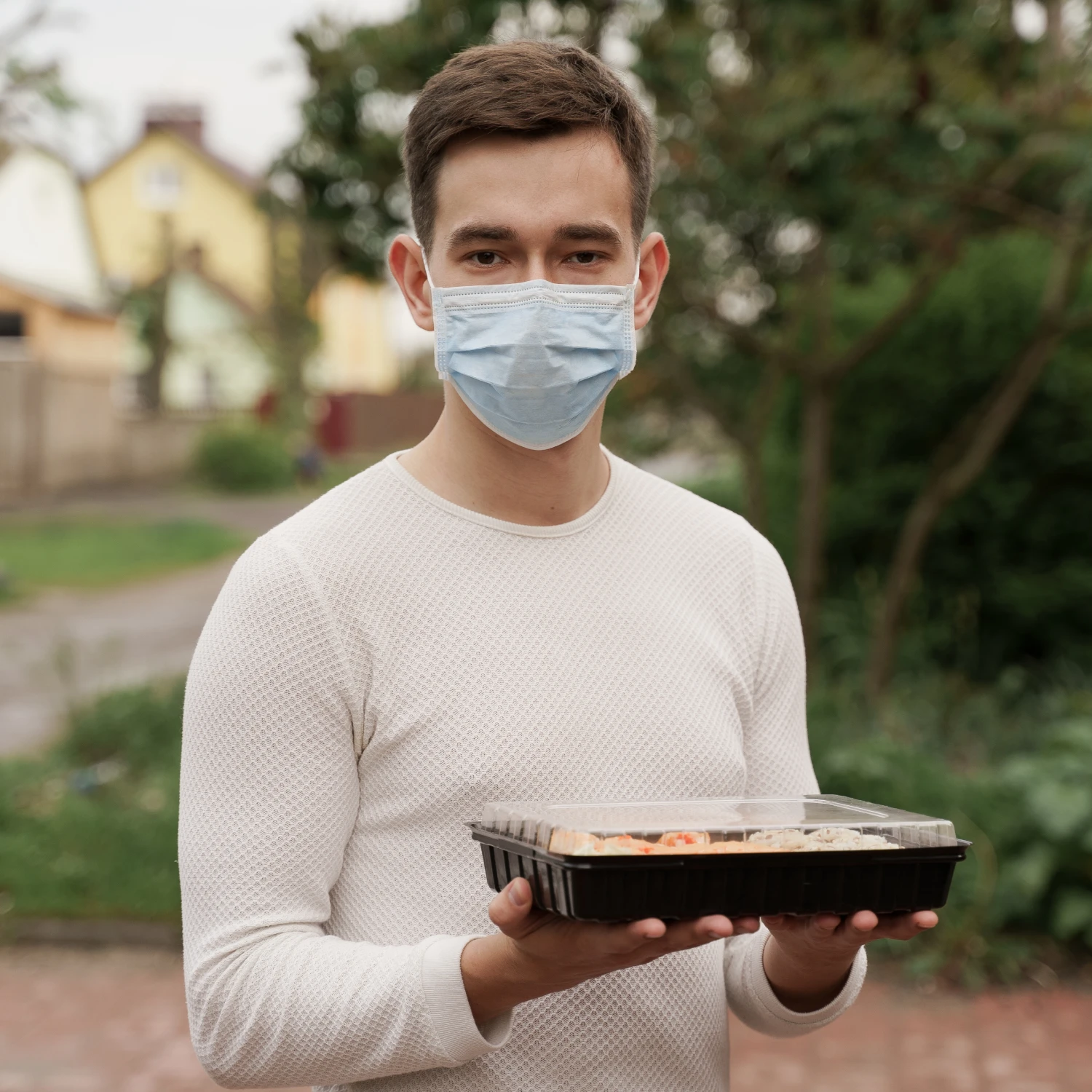 A man in a face mask holds a tray of food, ready to serve or present the meal.